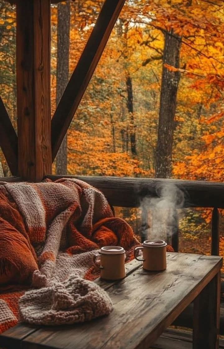 Cozy cabin porch with two steaming mugs overlooking autumn forest
