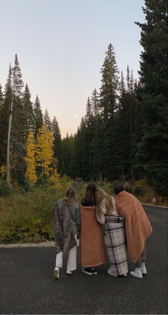 Women wrapped in blankets walking among the pines at dusk