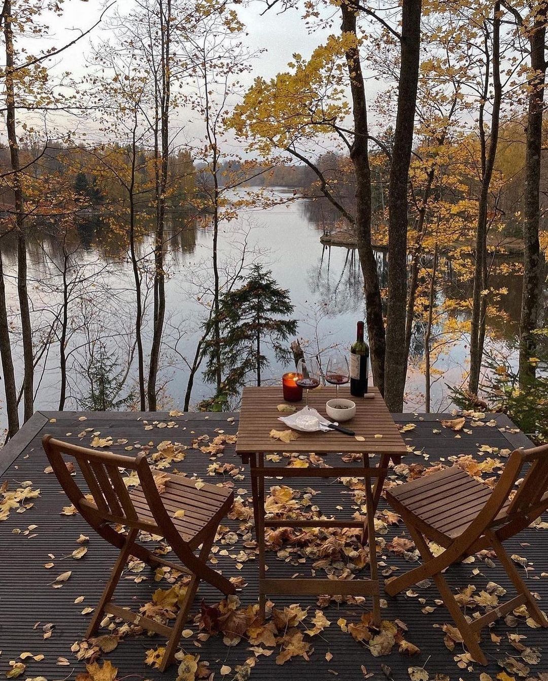Candlelit table for two on a lakeside deck strewn with autumn leaves